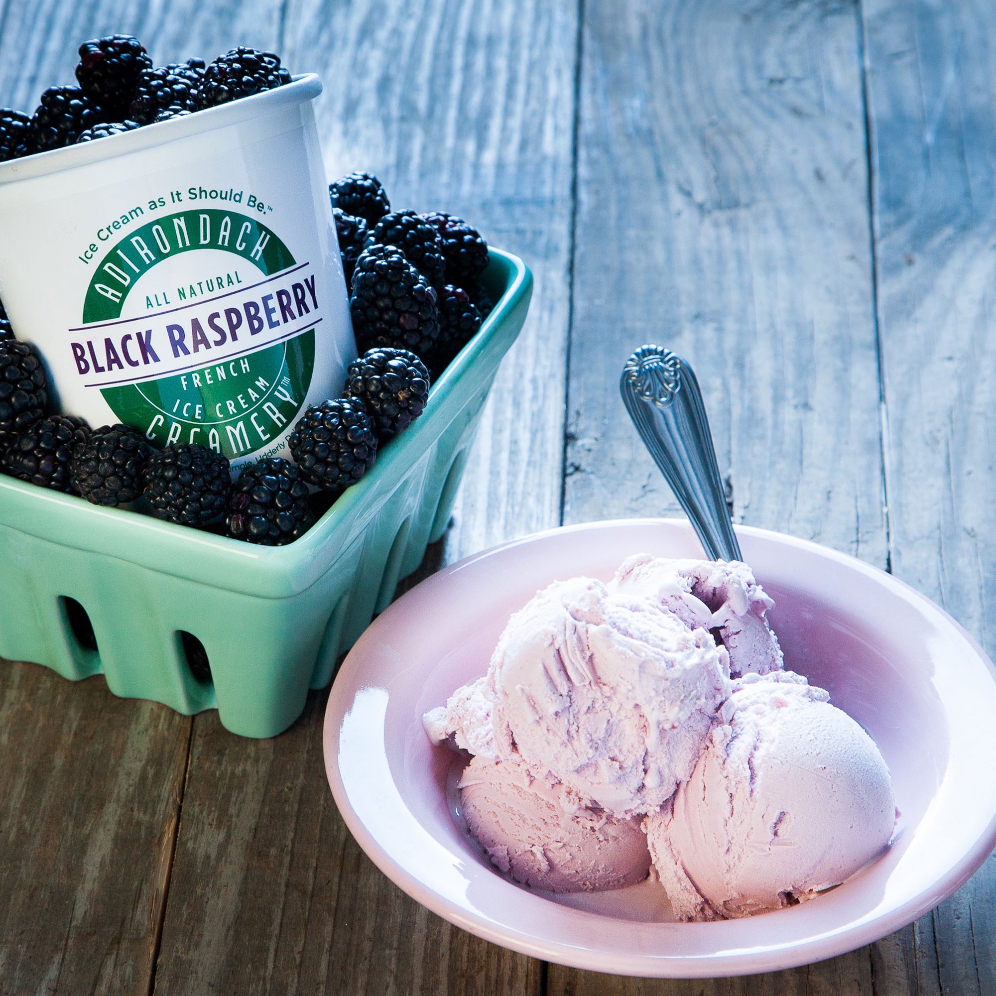Bowl of black raspberry ice cream with a container of black raspberries on a wooden surface