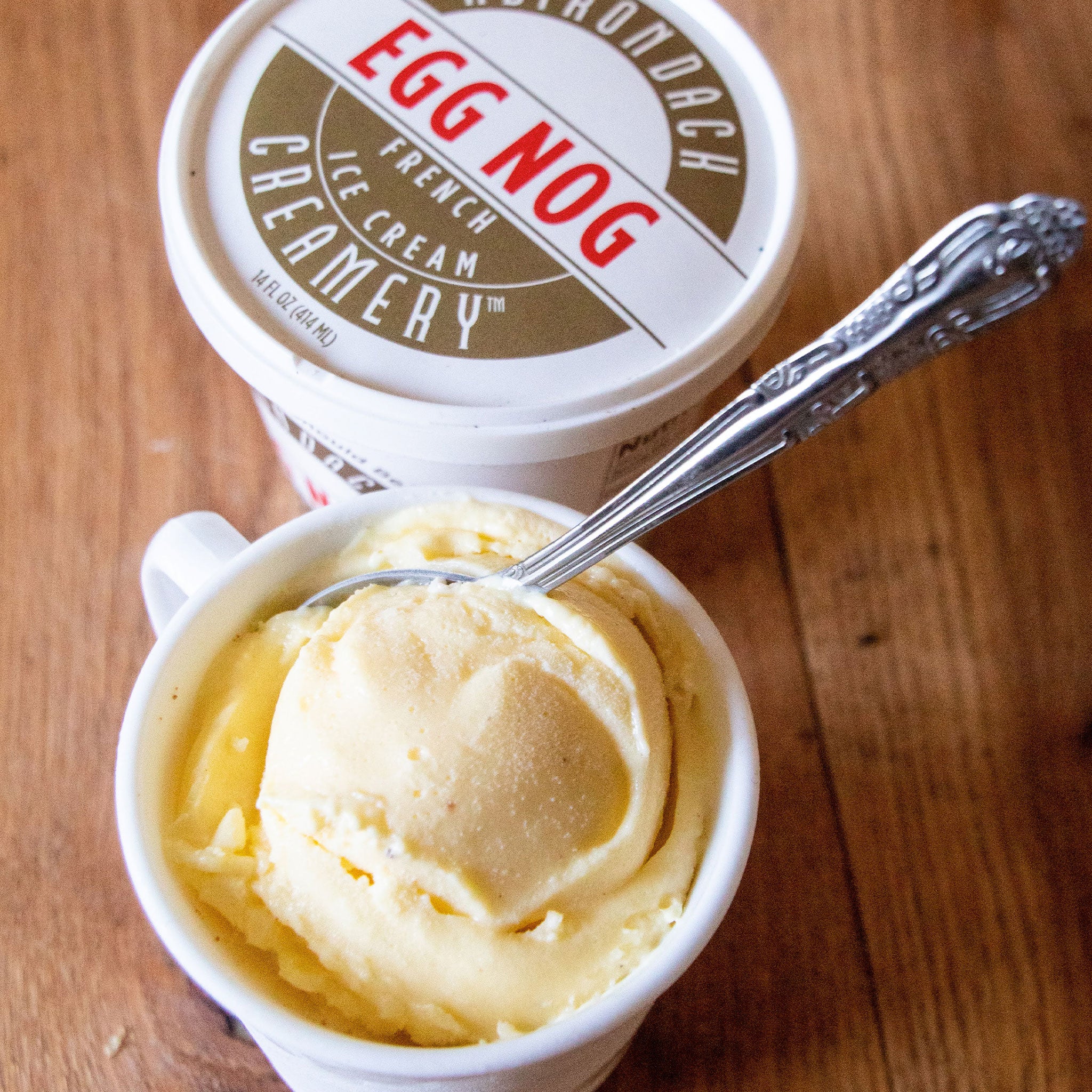 Egg nog ice cream in a container with a spoon on a wooden surface