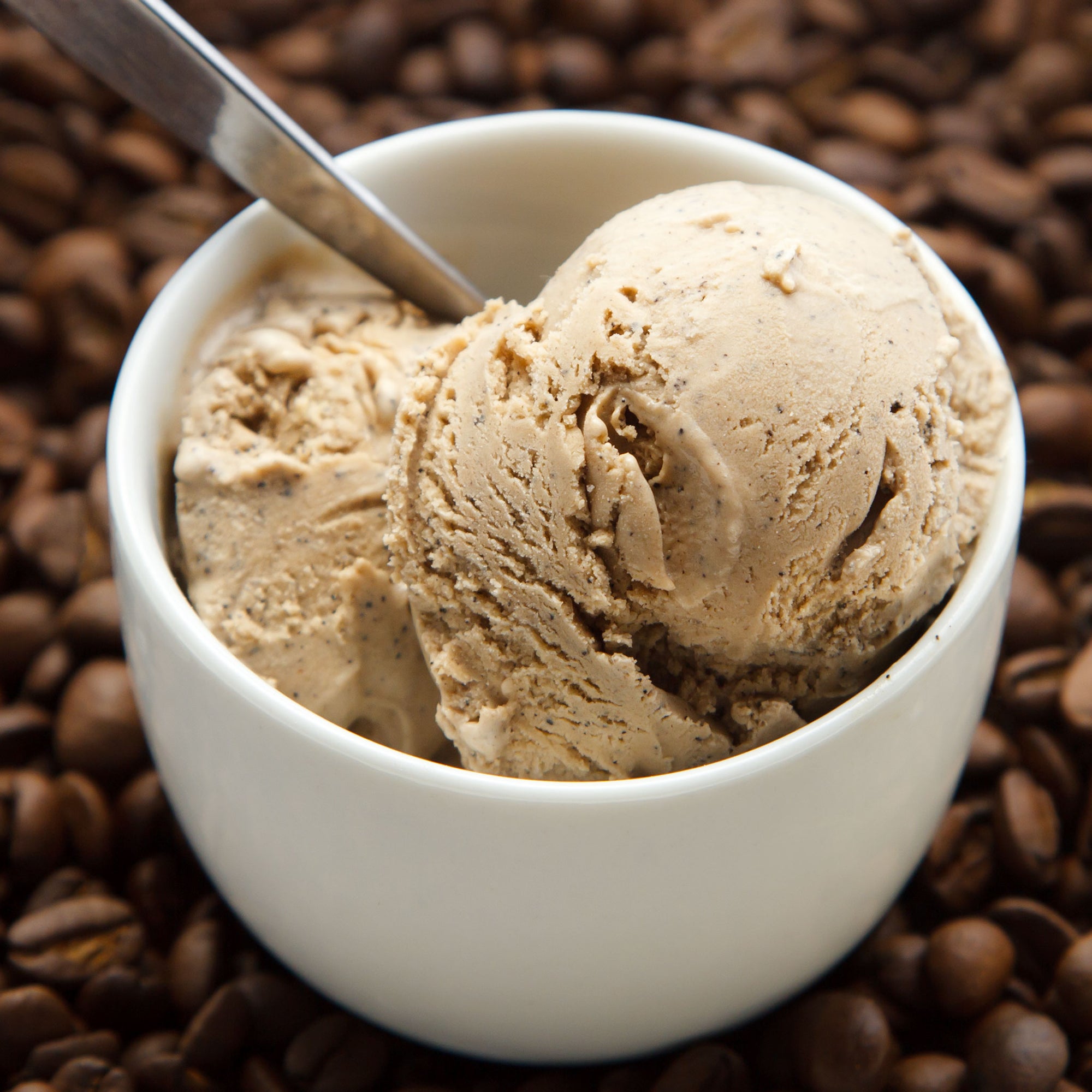 Two scoops of high peak perk ice cream in a white bowl with coffee beans around.