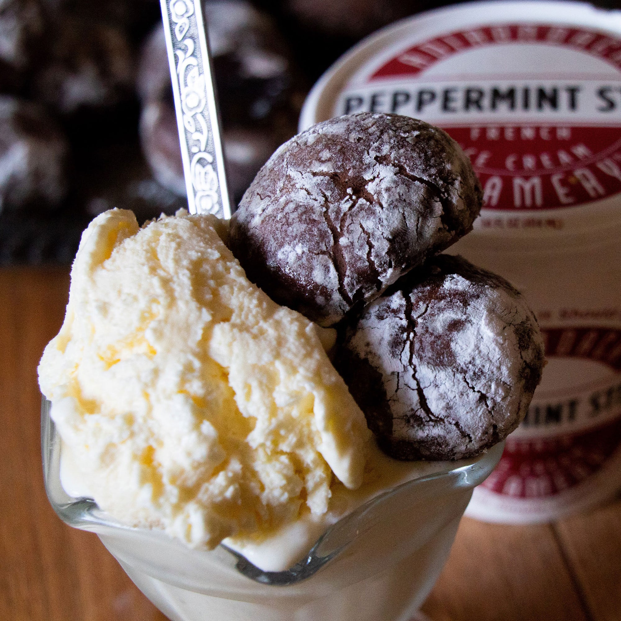 Peppermint Ice cream sundae with two chocolate cookies and a spoon, with a peppermint stick container in the background.
