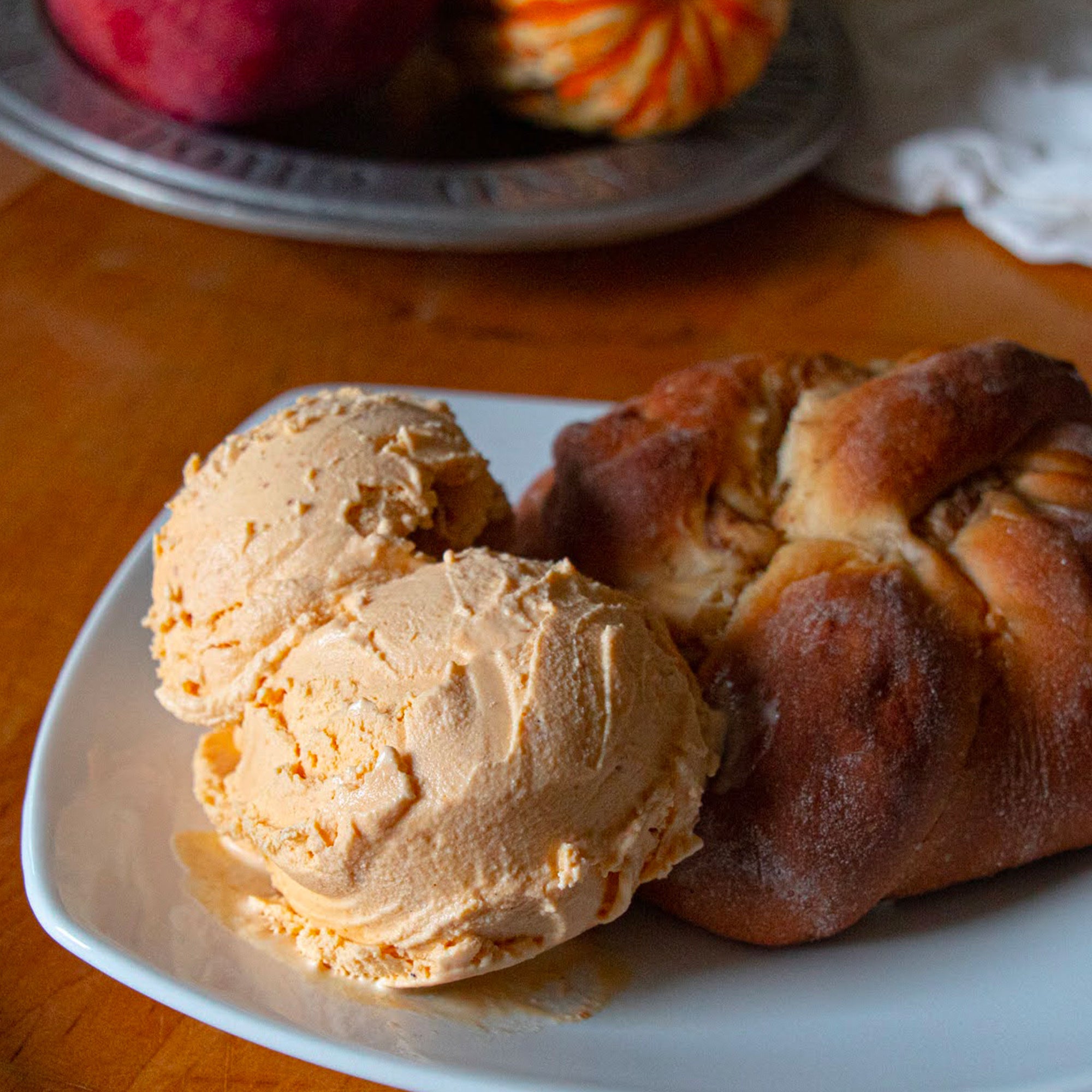 Two scoops of pumpkin ice cream and a pastry on a white plate with a wooden background.