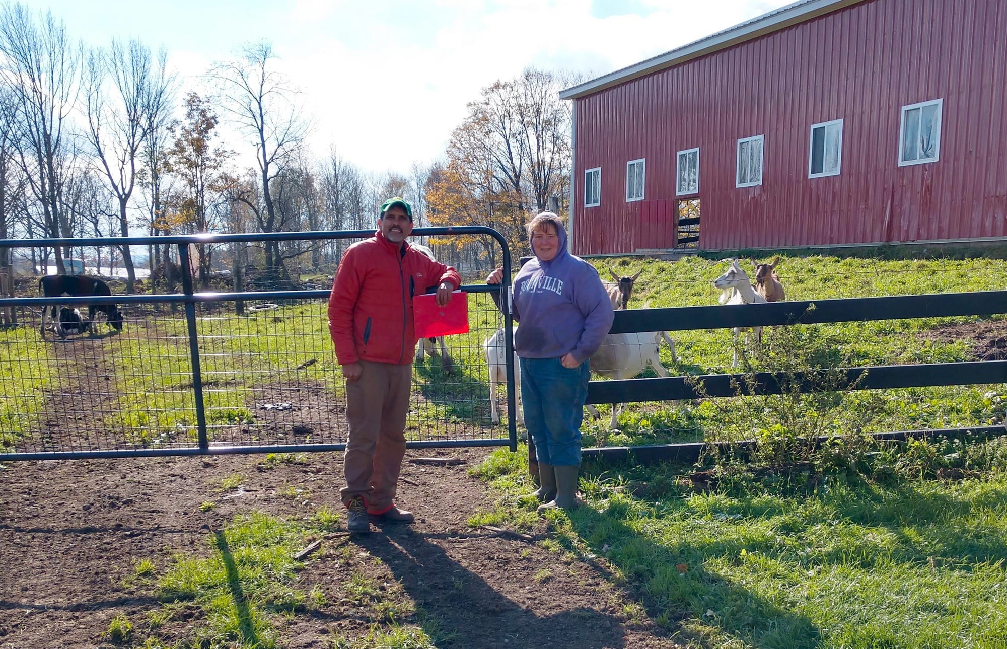 Paul and farm worker standing near a gate with a red barn in the background