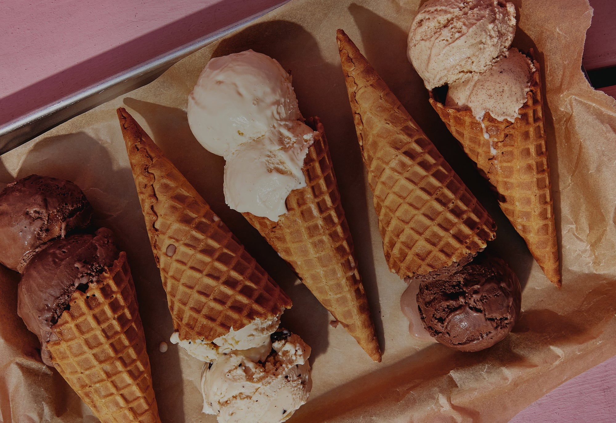 Ice cream cones with different flavors on a pink surface
